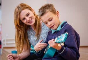 A student learns guitar with his music teacher.