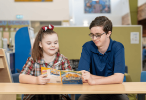 A photo of a School-Based Education Support (SBES) Trainee working with a happy student